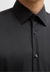 Camicia nera con bottoni, caratterizzata da una texture liscia, colletto a punta e chiusura con un solo bottone, dal design minimalista e senza motivi.