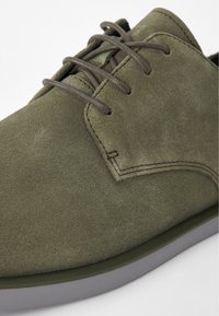 Scarpe in suede verde con una texture liscia, caratterizzate da una punta arrotondata, lacci piatti e una suola in gomma grigia a contrasto.