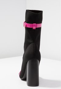 Mustat nilkkurit, joissa on teksturoitu neuleosa, vaaleanpunainen patenttista ankle-strap ja paksu musta korko. Sileä pinta ja istuva muoto.