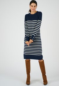 Abito a maglia a righe navy e bianche con maniche lunghe, caratterizzato da bottoni decorativi ai polsini e una vestibilità dritta, indossato con stivali al ginocchio in suede marroni.