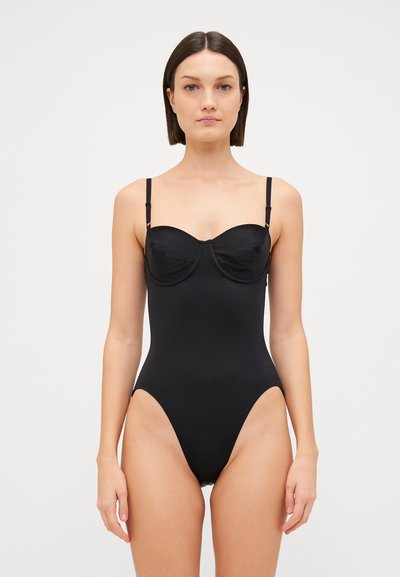 Zwarte badpak met een gestructureerde, gewatteerde bodice, dunne verstelbare schouderbandjes, hoge beenopeningen en een gladde matte textuur.