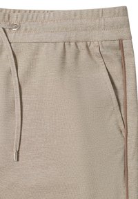 Beige leichte Stoffhose mit Kordelzug an der Taille, seitlichen Taschen und brauner Paspelierung entlang der Taschenkante.