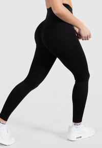 Leggings neri a coste a vita alta con una vestibilità aderente e una texture liscia, abbinati a sneakers sportive bianche con un sistema di ammortizzazione visibile.