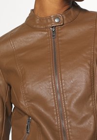 Veste en cuir marron avec un col montant, fermeture éclair à l'avant et poches latérales. Présente une texture lisse et une coupe ajustée.