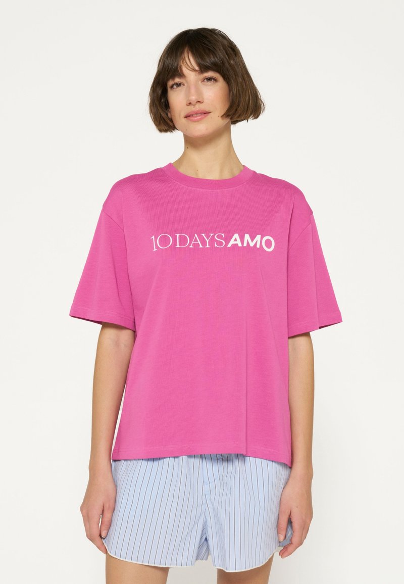Roze T-shirt met korte mouwen met de tekst "10 DAYS AMO" in het wit, gemaakt van een zachte stof. Draagt met blauw gestreepte shorts.
