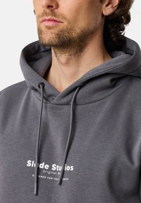 Felpa grigia con cappuccio, dotata di cordino, in tessuto morbido e con stampa "Slide Studios" sul davanti. Design semplice e rilassato.