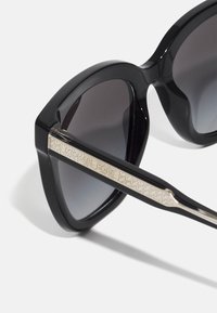 Black sunglasses with a thick frame and gray lenses. Silver metal accents on the temples feature the engraved text "MICHAEL KORS."