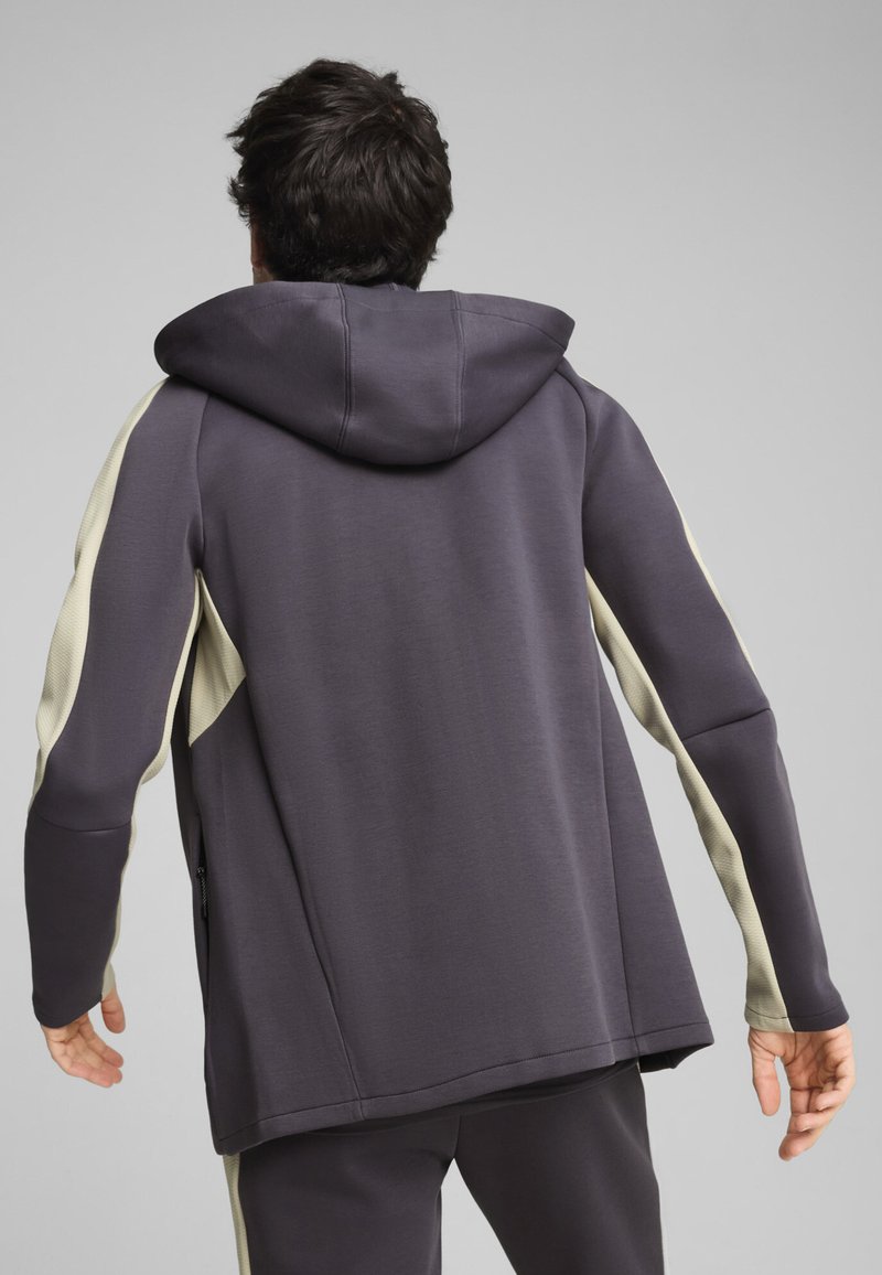 Chaqueta con capucha en gris oscuro con paneles laterales de color crema, que presenta una tela texturizada, mangas ajustadas y un corte relajado con un dobladillo recto.