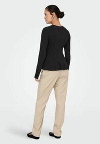 Black long-sleeve top with fitted design and seam detailing, paired with beige straight-leg pants and black flat shoes.