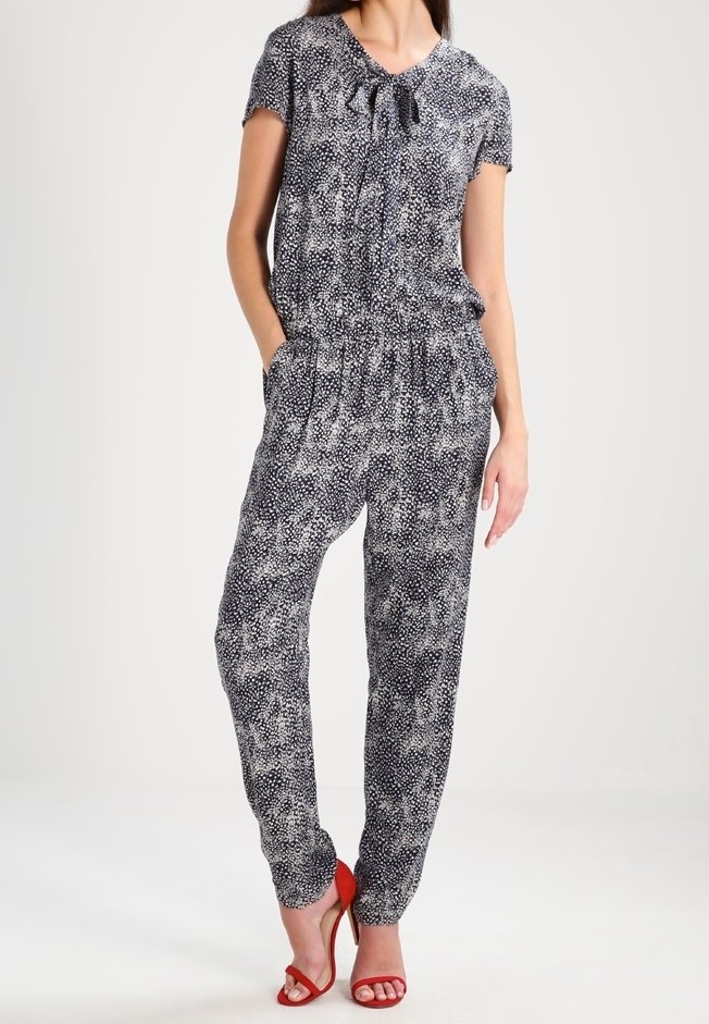 Granatowy kombinezon z rozrzuconym białym wzorem, krótki rękaw i wiązany dekolt. Posiada elastyczny pasek w talii oraz dwie boczne kieszenie. W połączeniu z czerwonymi sandałami.