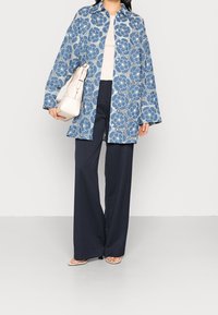 Abrigo de flores azules, realizado en un material ligero, combinado con pantalones anchos azul marino y un bolso beige.