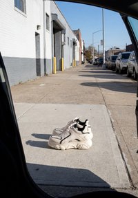 Paire de baskets blanches et noires laissée sur un trottoir en béton vide à côté d'une rue avec des voitures garées et des bâtiments en plein jour.