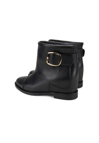 Bottes noires en cuir à la cheville avec un bout rond, présentant une large sangle et une boucle dorée sur le côté extérieur, des surfaces texturées et un talon bas.