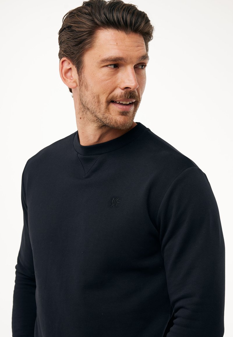 Granatowy sweter z okrągłym dekoltem, teksturowana tkanina i wytłaczany detal z logo na klatce piersiowej. Dopasowany krój z długimi rękawami.
