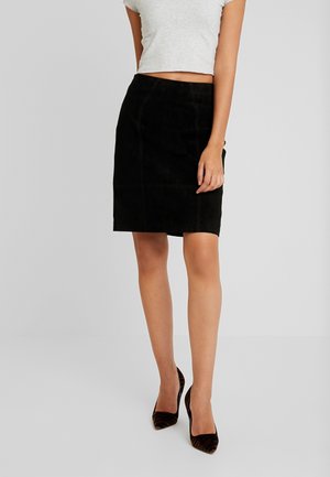 Sort suede blyantskirt med en glat tekstur, der har syninger og en tætsiddende design, parret med højhælede sko.