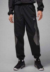 Black athletic pants with a shiny, smooth texture, featuring a dotted pattern on the sides and an elastic waistband.