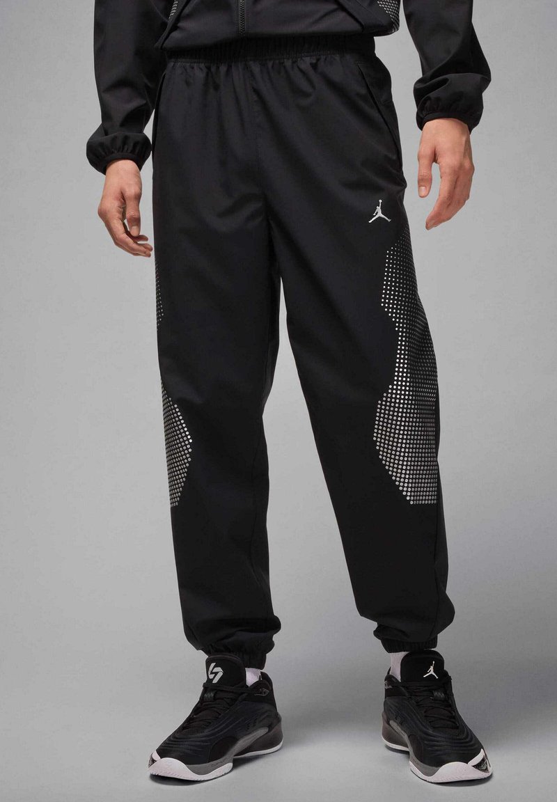 Black athletic pants with a shiny, smooth texture, featuring a dotted pattern on the sides and an elastic waistband.