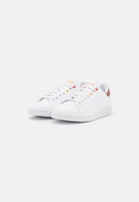 Vita sneakers med en slät läderöverdel, med perforeringar på sidorna, vita snören och en flerfärgad hälflik.