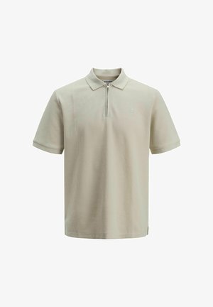Világos bézs színű polo ing, rövid ujjú, cipzáros záródás, textúrált anyag, diszkrét logó a mellrészen, és oldalt hasított a szegélyén.