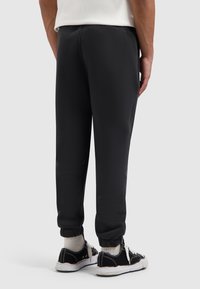 Zwarte joggerbroek met elastische boorden, een gladde textuur en een taps toelopend ontwerp, gecombineerd met zwarte sneakers en witte sportsokken.