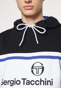 Mikina s kapucí v černé barvě, která má bílé a modré vodorovné pruhy. Obsahuje logo a šňůrku s bílými konci. Bavlněná tkanina.