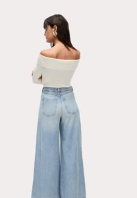 Blusa blanca sin mangas combinada con jeans de pierna ancha en azul claro. Los jeans tienen una cintura alta y dos bolsillos traseros.