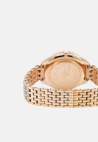Złoty zegarek z metalową bransoletą o splocie i gładką kopertą. Posiada mały kryształ na koronie oraz minimalistyczny design tarczy.