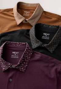 Trois polos pour hommes empilés. En haut : marron avec un col à motif. Au milieu : noir avec un col à motif ondulé. En bas : violet foncé avec un col fleuri.