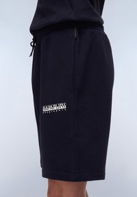 Shorts en coton bleu marine avec taille élastique, poches latérales et détails de logo blanc. Texture douce avec une coupe décontractée et une longueur au-dessus du genou.