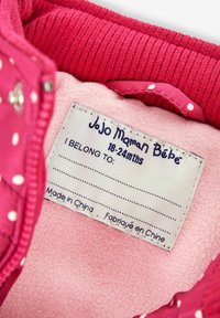 Różowa polarowa kurtka od wewnątrz, zawierająca metkę z napisem "Jojo Maman Bébé", rozmiar 18-24 miesiące, pustą przestrzenią na dane właściciela oraz napisem "Wyprodukowano w Chinach".