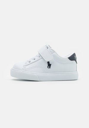 White synthetic sneakers with a velcro strap and lace design. Features a textured sole, small logo on the side, and a contrasting heel accent.