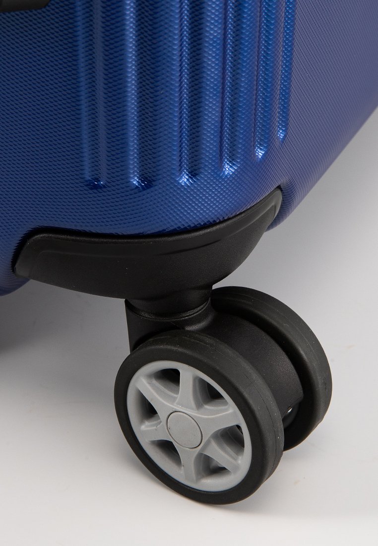 Maleta rígida azul con superficie texturizada, surcos verticales y una base de plástico negro. Cuenta con una única rueda giratoria gris.