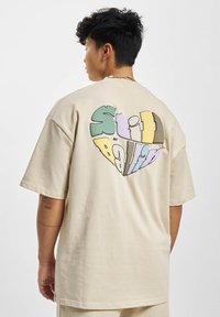 Beige bomulds oversized t-shirt med et farverigt grafisk tryk med teksten "Still Ballin'" bagpå, med en afslappet pasform og korte ærmer.