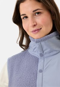 Helllila Weste mit Fleece-Struktur auf der Vorderseite und glattem Stoff auf der Rückseite, hohem Kragen und Druckknöpfen.