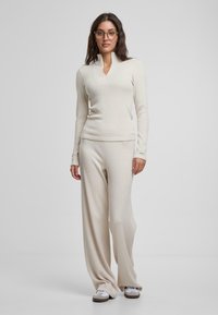 Pull en tricot crème à col montant avec manches longues, associé à un pantalon crème ample et des baskets grises. Tissu simple et texturé avec des lignes épurées.