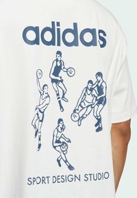 Bílá bavlněná tričko s námořnickými grafickými prvky pěti basketbalistů v akci, s textem "adidas" a "SPORT DESIGN STUDIO" pod ním.