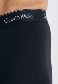 Zwarte Calvin Klein tailleband met witte logo-tekst, strakke pasvorm gemaakt van rekbare stof, gladde textuur en een middelhoog silhouet.