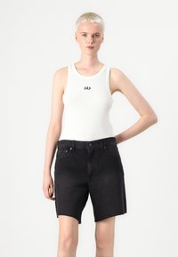 Débardeur blanc à côtes avec logo "GAP", associé à un short en denim noir avec une taille brute et un design classique à cinq poches.