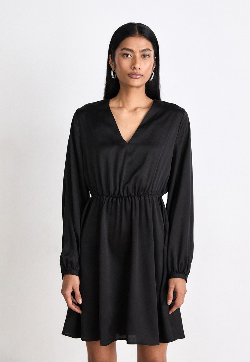 Black dress made of smooth fabric, featuring a deep V-neck, long sleeves, elastic waist, and a flared skirt. Simple and elegant design.