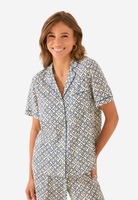 Korte mouwen, overhemd met knopen in roomkleur met een blauw geometrisch patroon, voorzien van een borstzak en een losse pasvorm. Gladde stoftextuur.