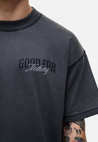 Czarna bawełniana koszulka z krótkim rękawem, z napisem "GOOD FOR Nothing" w kontrastowych stylach z przodu. Gładka tekstura.