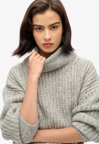 Chunky knit sweater in light grey with a high, folded turtleneck. Features rolled sleeves and a textured pattern. Soft fabric.