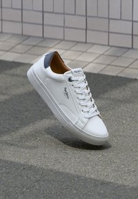 White sneaker with a smooth leather upper, gray heel accent, round toe, and textured rubber sole; features flat laces and branded detailing.