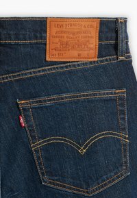 Jeans Levi's 511 in denim blu scuro, con una patch in pelle marrone con dettagli del marchio, cuciture arancioni e un design distintivo della tasca posteriore.