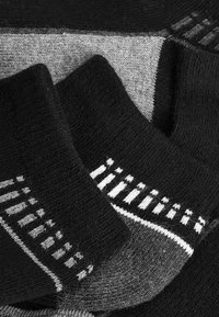 Schwarze und graue Socken mit strukturiertem Strick. Enthält ein Streifenmuster in Weiß nahe dem Bündchen. Weicher Stoff in verschiedenen Grautönen.