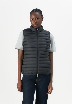 Zwarte gewatteerde vest met hoge kraag, ritssluiting met een oranje treklabel, gedragen over een grijs T-shirt met korte mouwen, gecombineerd met donkere jeans.