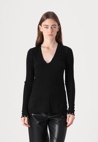 Pull à manches longues noir côtelé avec un décollet�é en V, présentant des lignes verticales texturées et des accents de boutons sur les poignets.