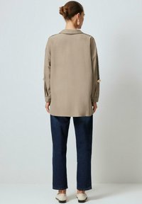 Jasno beżowa koszula casualowa z długimi rękawami i zapięciem na guziki, zestawiona z ciemnoniebieskimi jeansami prosto nogami i beżowymi butami. Minimalistyczny design.