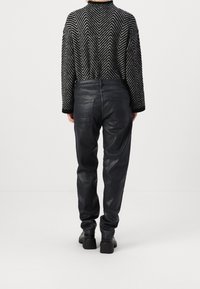 Pantalones de cuero negro con una textura suave, con un diseño entallado y bolsillos traseros, combinados con un suéter estampado en blanco y negro.