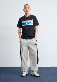 Svart t-skjorte med multicolor grafikk og Nike-logo, paret med lysegrå joggebukser med svarte sidestykker og logopatch.